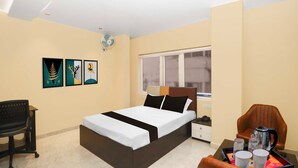 A hotel room with a bed, a desk, a chair, a bedside table, a window, and artwork on the wall. - Townhouse Ranchi Tapovan Mandir (Ranchi)