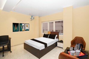 Habitación de hotel con cama, escritorio, silla, mesita de noche, ventana y una obra de arte en la pared.