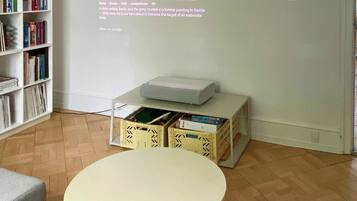 Een kamer met een witte muur, een boekenkast, een tafel en een beamer die een Netflix-interface toont.