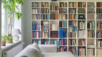 Een woonkamer met een grote boekenkast, een bank, een lamp en een potplant.
