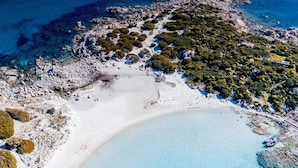 Vista aèria d'una platja amb aigües blaves cristal·lines, roques i vegetació escassa.