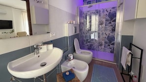 Un bany amb rentamics, vàter, bidet i plat de dutxa amb cortina de flors.