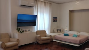 Habitació d'hotel amb un llit, una taula de treball, una cadira, un televisor i un quadre al mur.