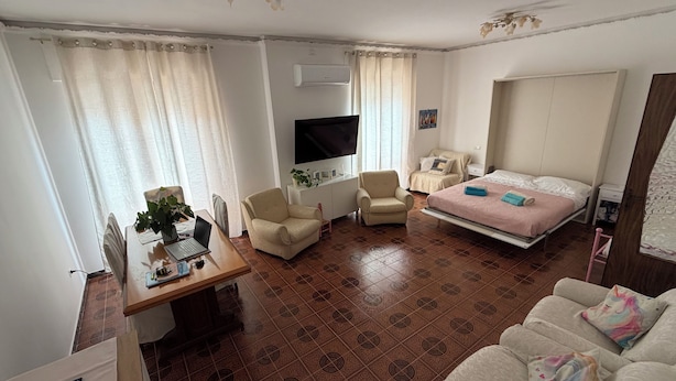 Habitació d'hotel amb un llit, dues butaques, una taula de treball amb un ordinador portàtil, una televisió i un paviment amb dibuixos.