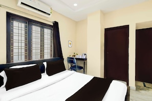 Habitación de hotel con cama, escritorio con silla, unidad de aire acondicionado y puerta.