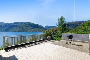 A deck with a view of a lake and mountains, a barbecue grill, and a potted plant.