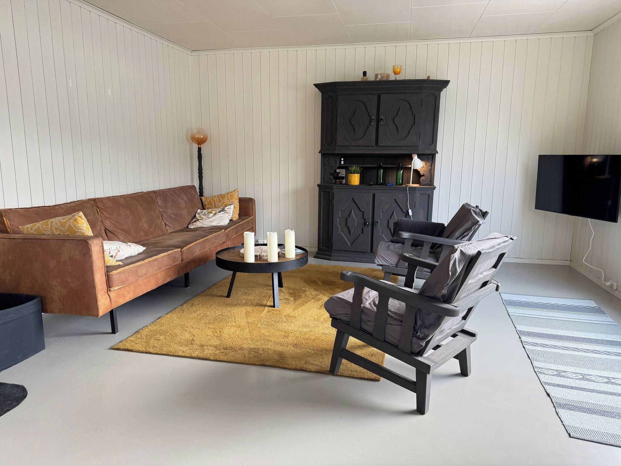 A living room with a brown sofa, a round coffee table, a dark wooden cabinet, and a television mounted on the wall.