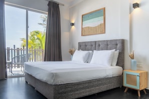 Une chambre à coucher avec un lit, une table de chevet, un tableau et une vue sur des palmiers.