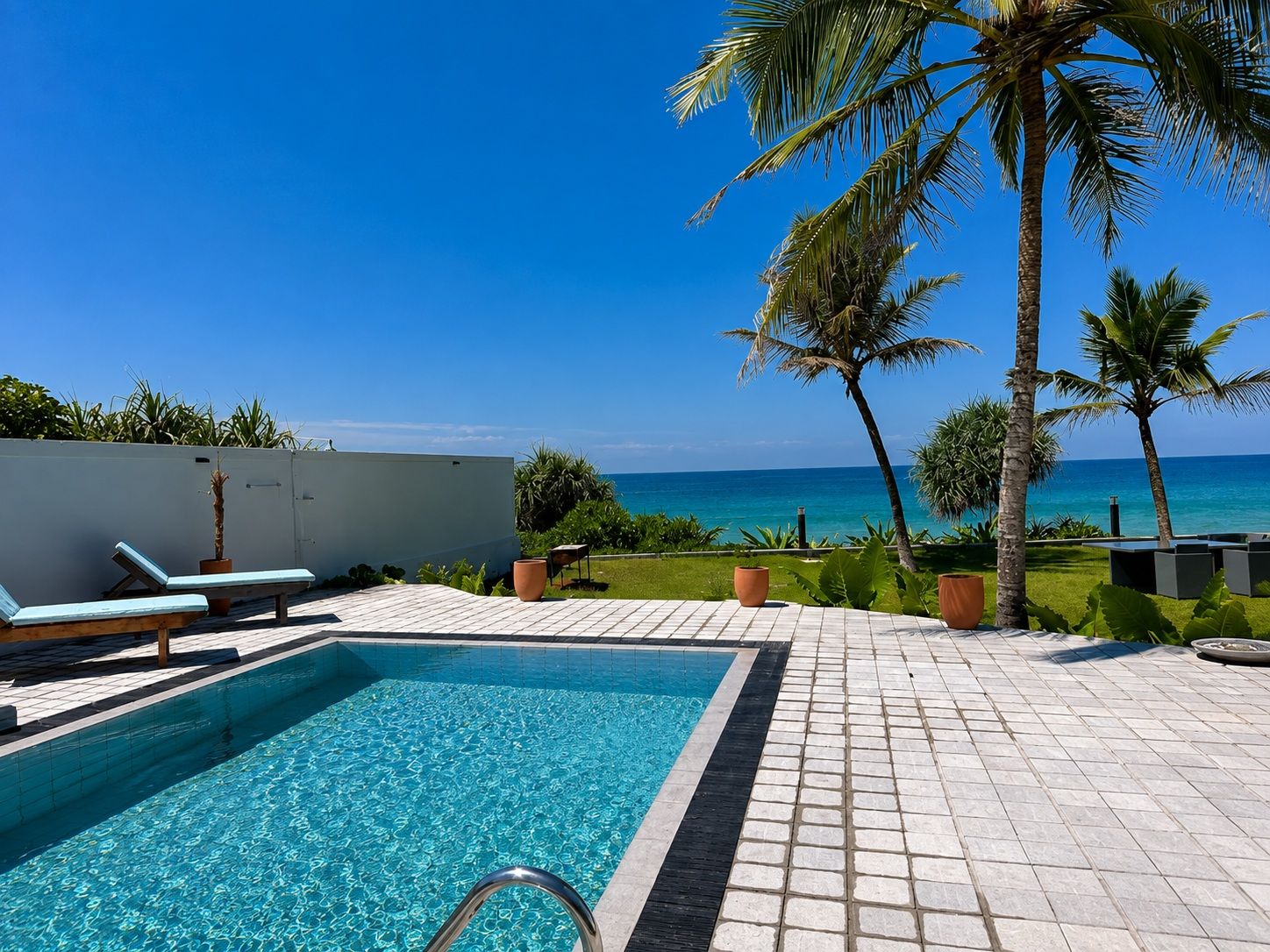 Une piscine avec vue sur l’océan, entourée de palmiers et de chaises longues.