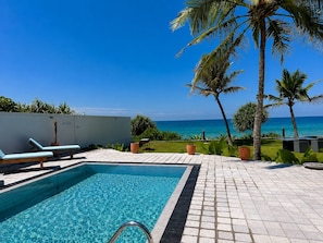 Une piscine avec vue sur l’océan, entourée de palmiers et de chaises longues.