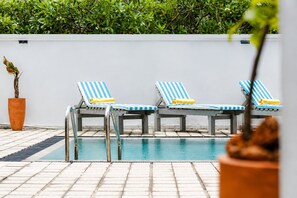 A poolside area with three striped lounge chairs, a potted plant, and a tiled deck.