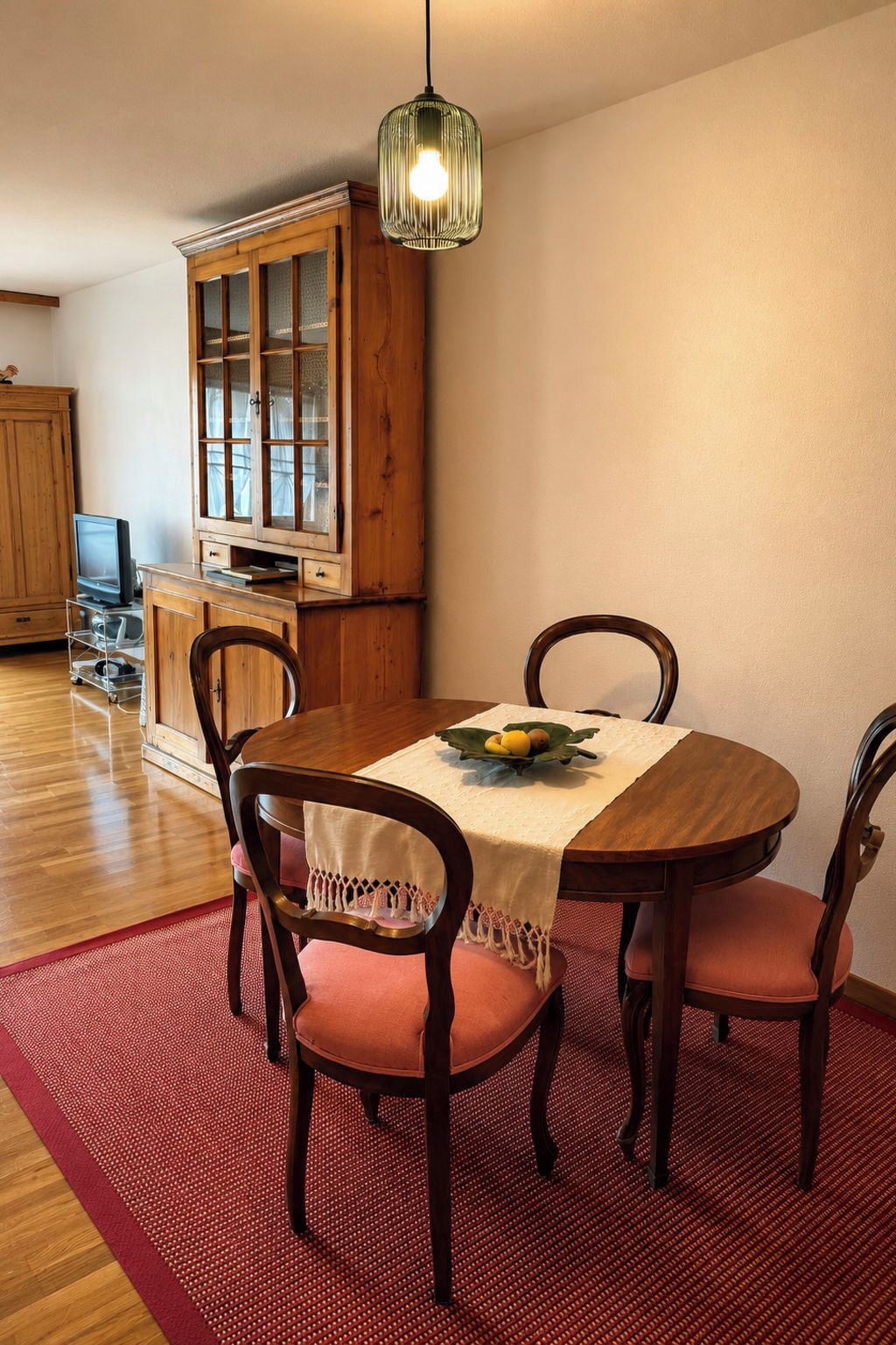 Een eetruimte met een houten tafel, vier stoelen, een fruitschaal en een hanglamp.