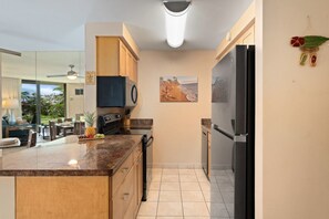 A modern kitchen with a central island, a refrigerator, and a dining area with a view. - Beach Front & Just Steps to Pools & Hot Tub (Kihei)