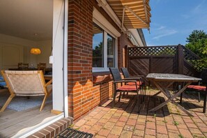Eine Terrasse mit Tisch und Stühlen, ein Holzzaun und eine Ziegelwand.
