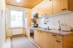 A kitchen with wooden cabinets, a stove, a sink, and a window with curtains. - 2 in the house Sturmmöwe (ID 120) (St. Peter-Ording)