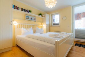 A bedroom with a bed, bedside lamps, a window, a radiator, and a bookshelf with books and plants. - 6 in the house at Blanker-Hans-Weg 5 (ID 084) (St. Peter-Bad)