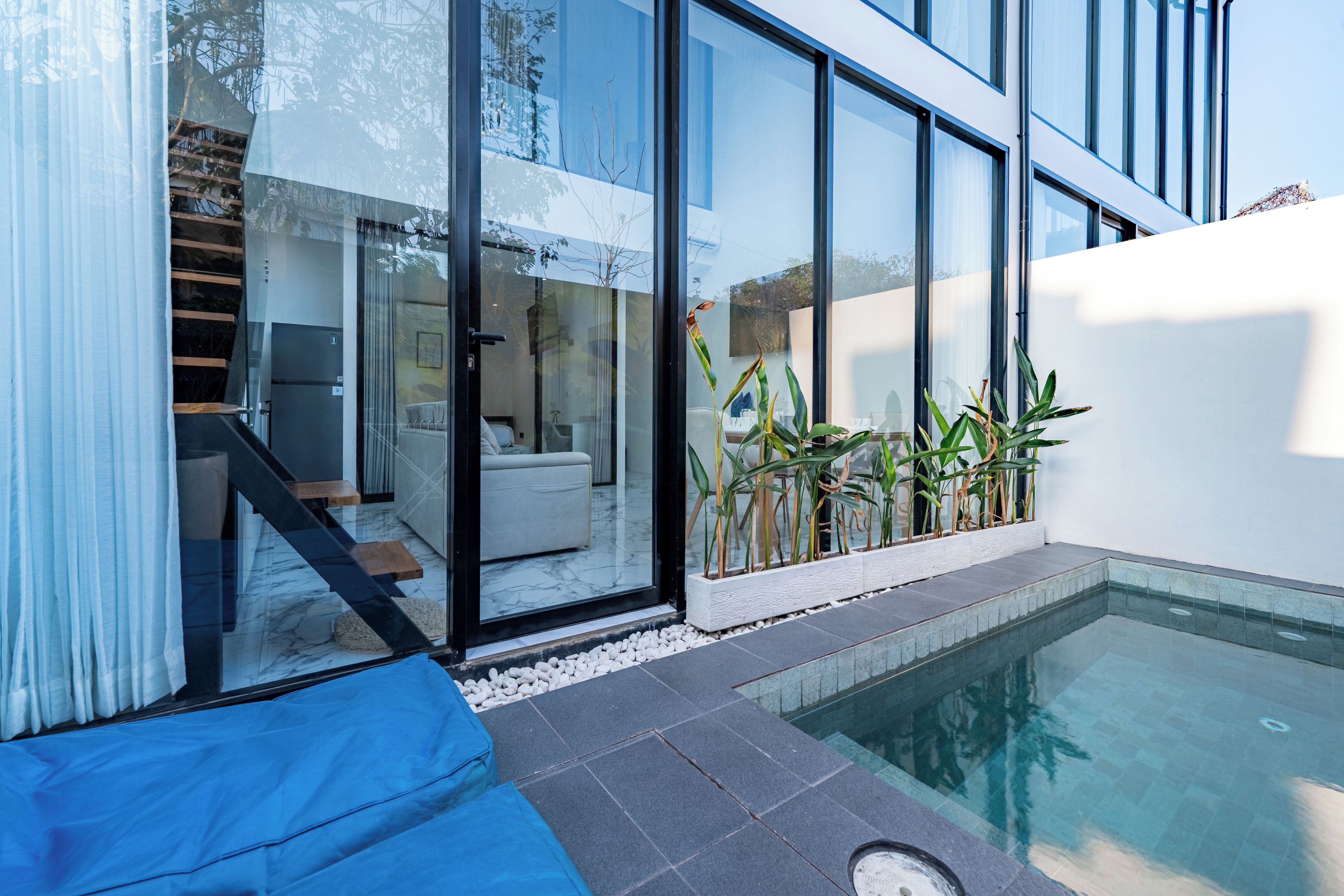 A modern outdoor pool area with a glass-enclosed patio, a blue sofa, and a staircase leading to an upper level.