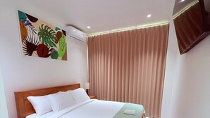 A hotel room with a wooden bed, a green throw blanket, a marble-patterned floor, a ceiling fan, and a wall-mounted TV. - Sun On the Hill Villa by Betterplace (Nusa Dua)