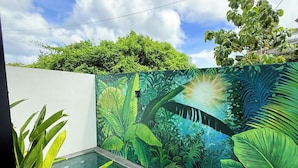 A swimming pool with a tropical mural on the wall, surrounded by greenery. - Sun On the Hill Villa by Betterplace (Nusa Dua)