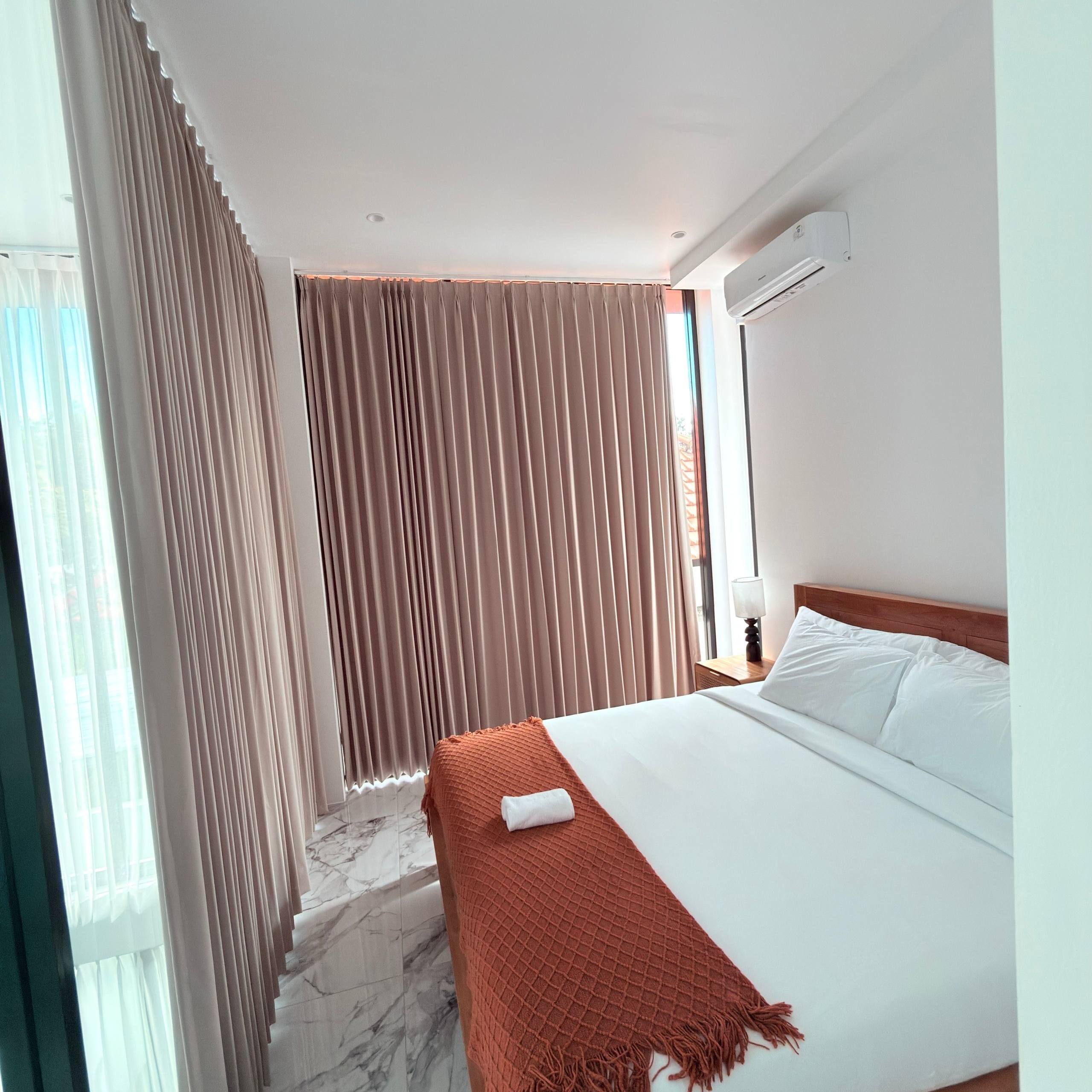 A hotel room with a bed, a nightstand, a lamp, and a window with curtains.