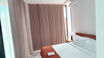 A hotel room with a bed, a nightstand, a lamp, and a window with curtains.