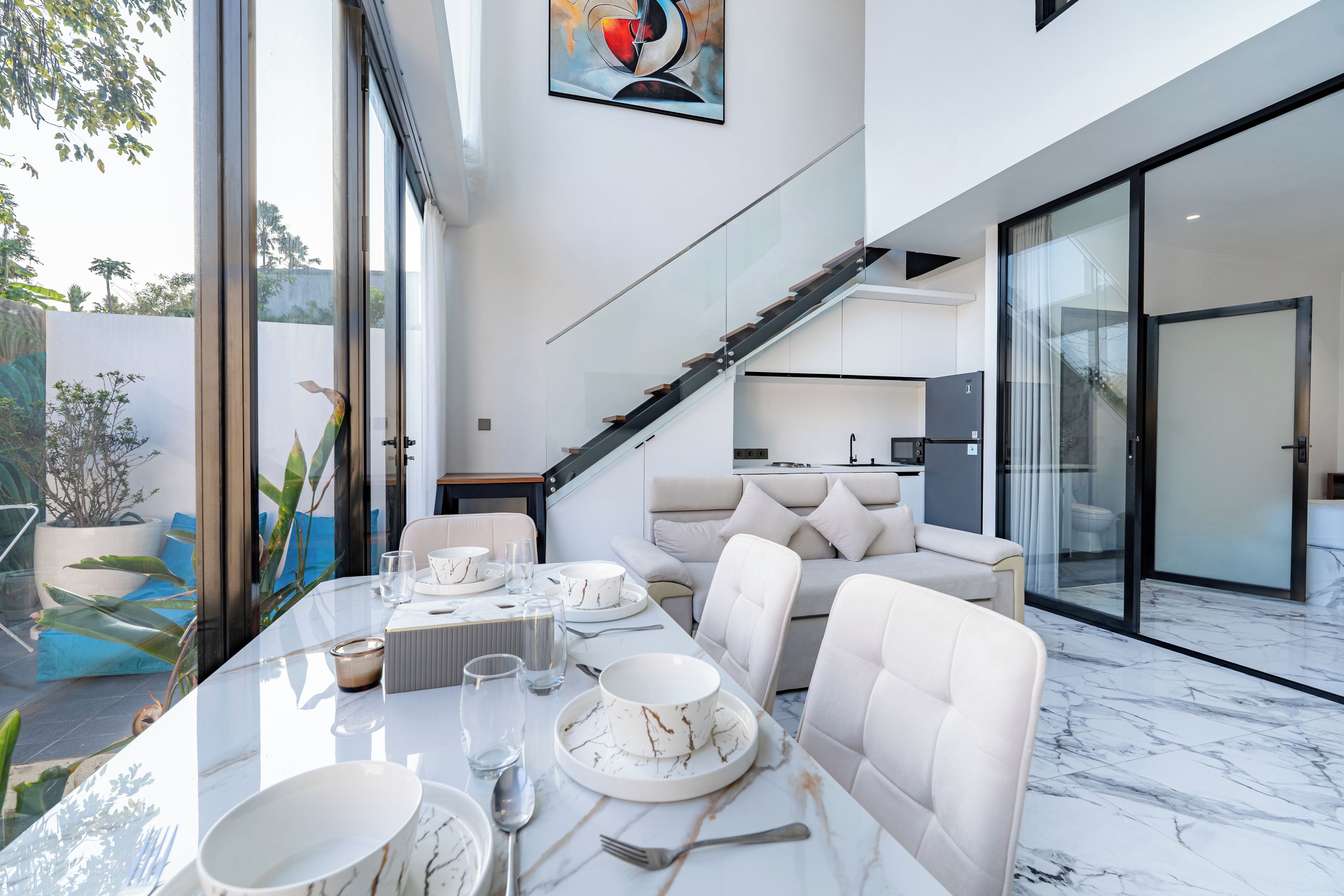 A modern interior with a dining area, a sofa, and a staircase leading to an upper level.