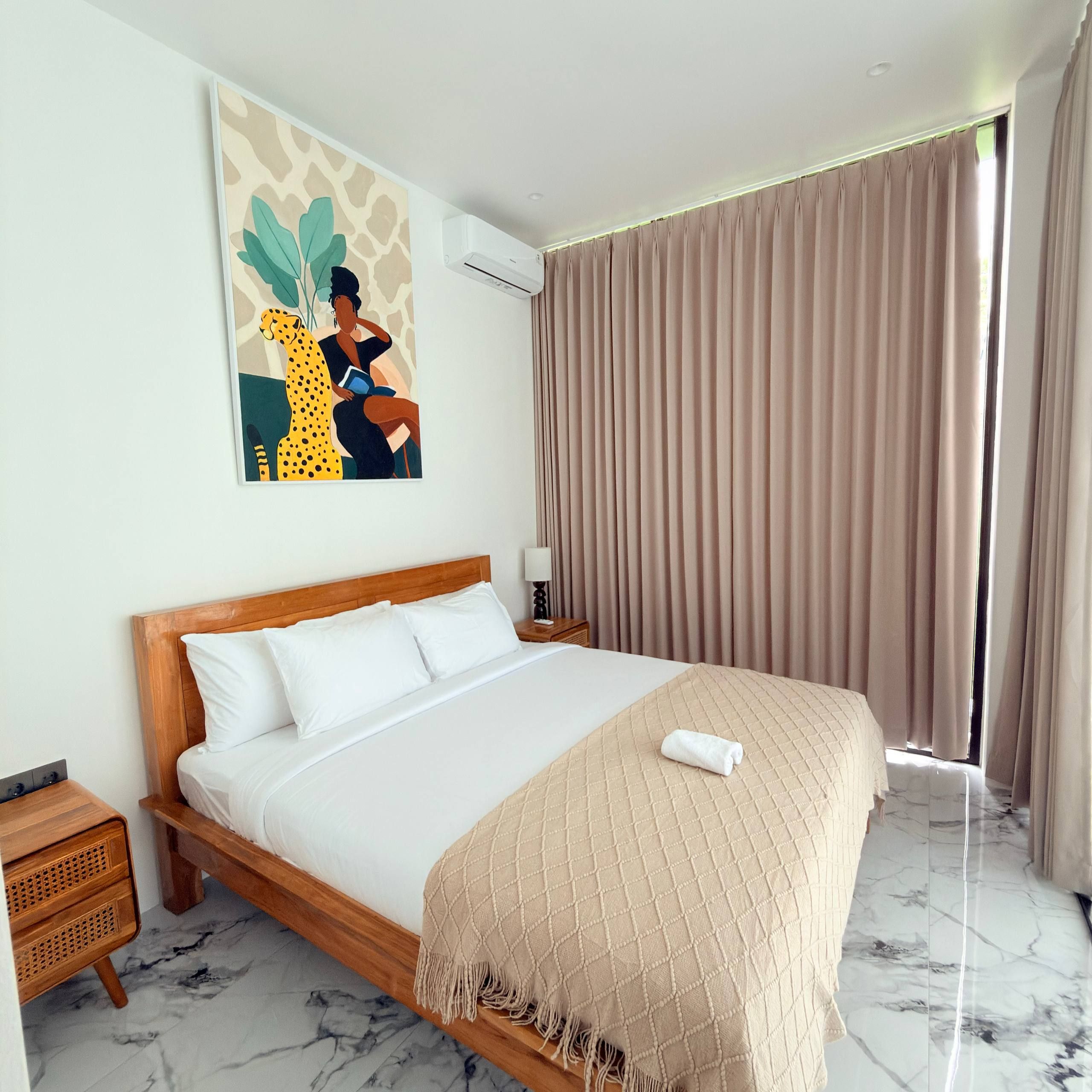 A hotel room with a bed, a nightstand, a lamp, a painting, and a window with curtains.