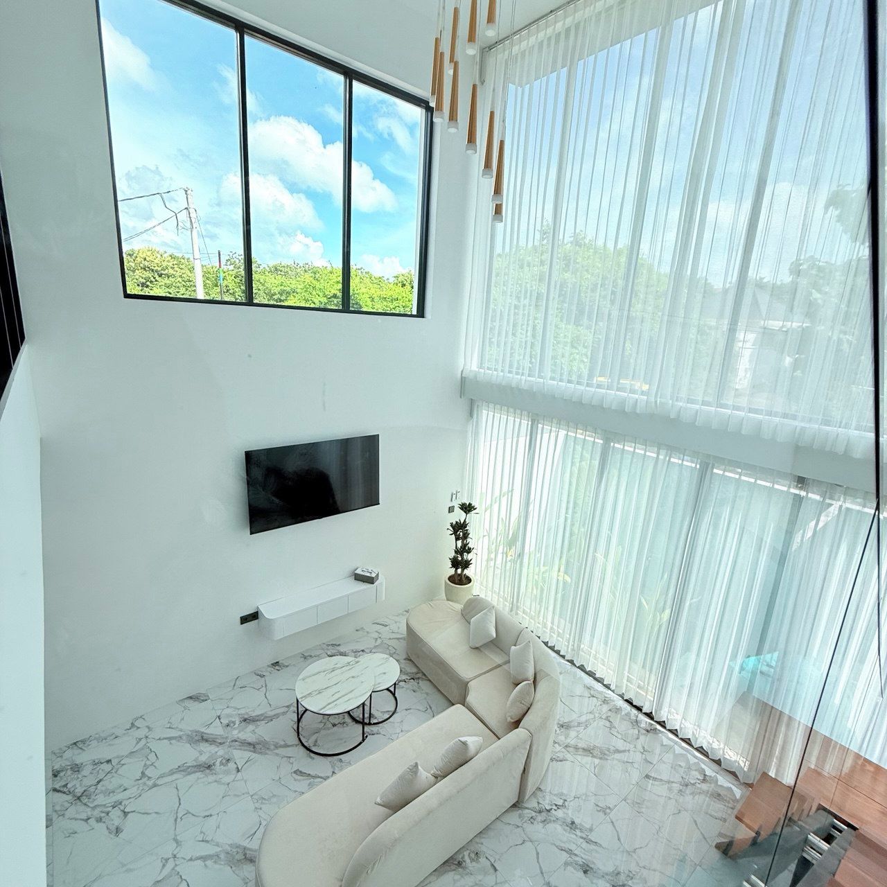 Una sala moderna con un ventanal grande, un televisor de pantalla plana, un sofá, una mesa de centro y una planta en maceta.