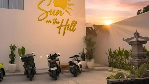 A building with a sign reading 'Sun on the Hill' and a sunset in the background. There are three motorcycles parked in front. - Sun On the Hill Villa by Betterplace (Nusa Dua)