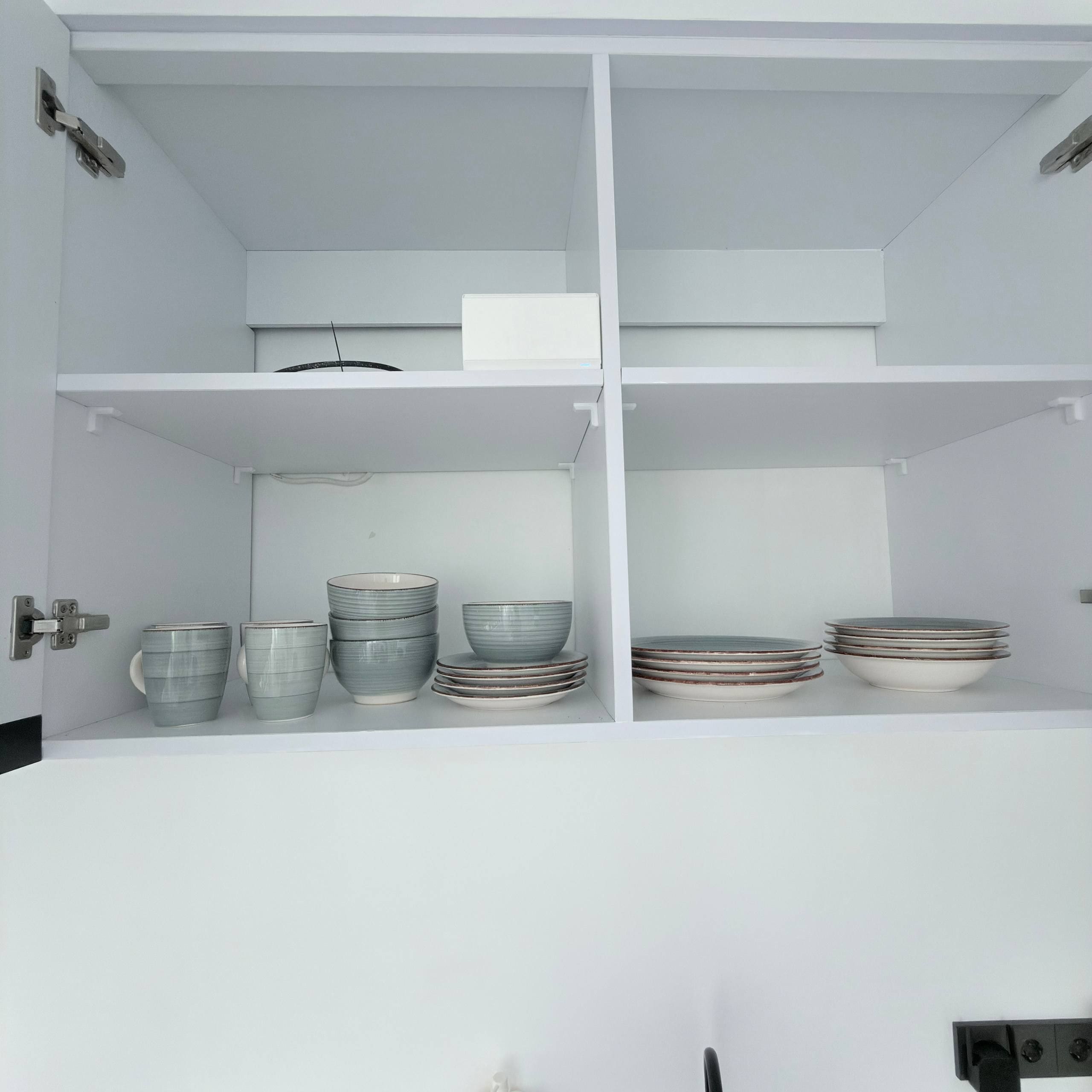 Une cuisine avec des armoires et des étagères blanches, contenant divers plats et ustensiles de cuisine.