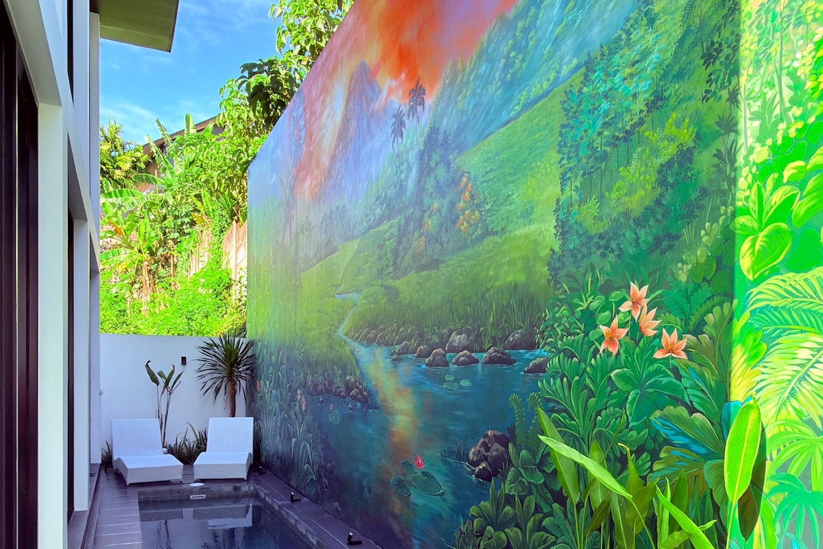 Área externa moderna com piscina, um mural de paisagem tropical e um espaço de estar com espreguiçadeiras brancas.