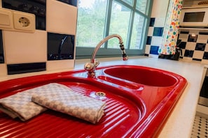 A red kitchen sink with a faucet, a towel, and a window with a view of trees. - Ground floor in the Reimer house (ID 312) (St. Peter-Ording)