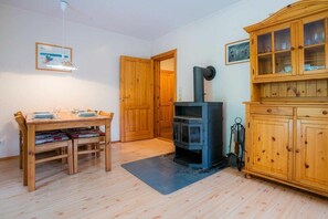 A room with a wooden table, chairs, a black stove, a cabinet, and a door. - Ground floor in the Reimer house (ID 312) (St. Peter-Ording)