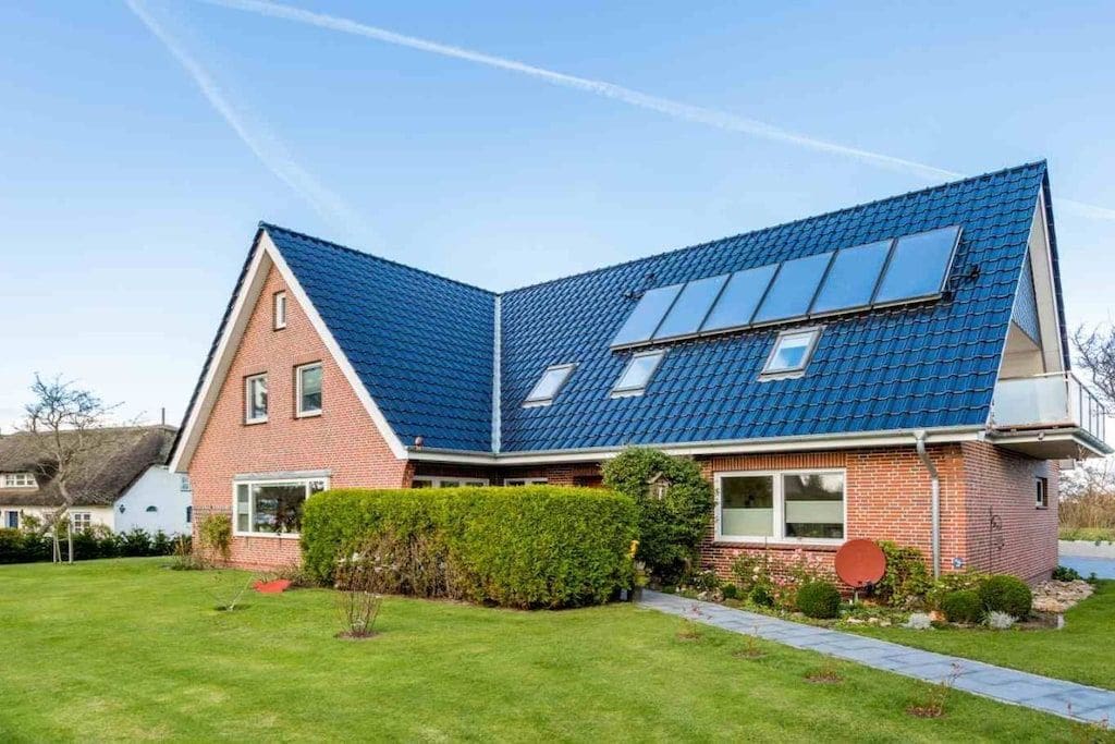 A house with a sloped roof, solar panels, a brick exterior, and a well-maintained lawn.