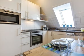 Eine moderne Küche mit weißen Schränken, einem eingebauten Backofen, einer Mikrowelle und einem Oberlicht.