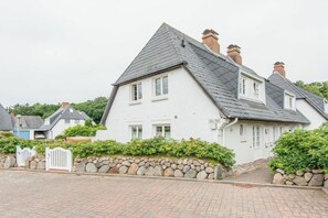 Ein weißes, zweistöckiges Haus mit einer Steinmauer und einem weißen Tor.