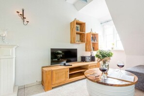 Ein modernes Wohnzimmer mit einem Flachbildfernseher, Holzmöbeln, einem runden Couchtisch und einer Topfpflanze.