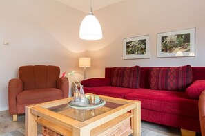 Un salón con un sofá rojo, una mesa de centro de madera, un sillón rojo y dos cuadros enmarcados en la pared.
