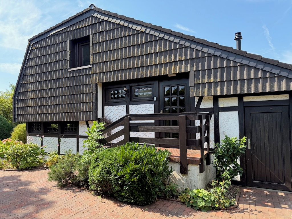 Ein traditionelles Haus mit einem Satteldach, einer Holztreppe, die zum Eingang führt, und einem Ziegelweg.