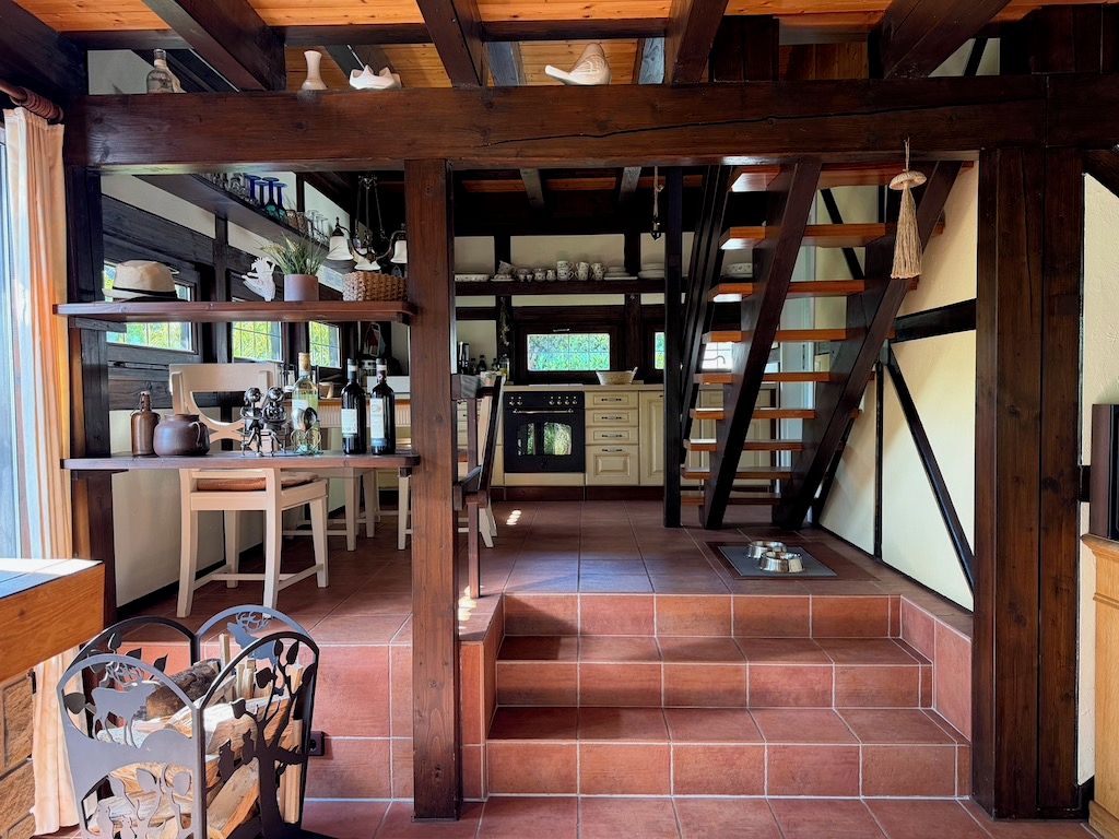 Ein rustikales Interieur mit einer Holztreppe, die zu einer Küche, einem Esstisch mit Stühlen und einem Kamin führt.