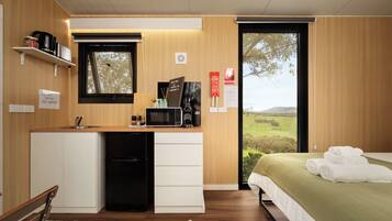 Ein kompaktes Hotelzimmer mit Küchenzeile, einem Bett mit grüner Bettdecke und Blick auf die Landschaft durch ein großes Fenster.