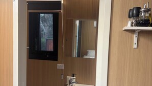 Une petite salle de bain comprenant des toilettes, un lavabo et un miroir. On y trouve une étagère avec des bouteilles et un petit meuble de rangement.