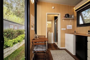 A compact kitchen with a dining area, a small refrigerator, and a window overlooking greenery.