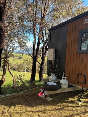 Un bâtiment avec une bouteille de gaz et un pneu posés sur le sol, entouré d’arbres et d’un champ d’herbe.