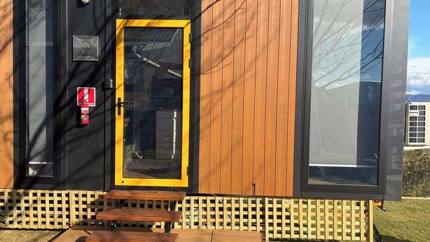 Un bâtiment moderne avec une façade en bois, une porte jaune et un extincteur fixé au mur.