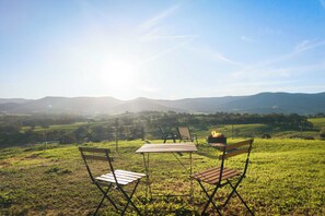 Un área de estar al aire libre con césped, una mesa, sillas, una fogata y vistas panorámicas de colinas y montañas.