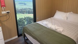 Une chambre d’hôtel avec un lit, une fenêtre donnant sur un paysage verdoyant et une couverture anti-feu accrochée au mur.