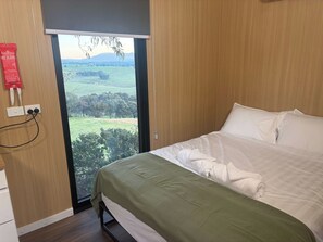Habitación de hotel con cama, ventana con vistas a un paisaje verde y una manta ignífuga en la pared.