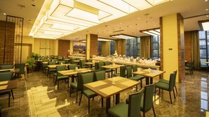 Un amplio comedor de hotel con varias mesas y sillas, una barra de buffet y grandes ventanales que permiten la entrada de luz natural.