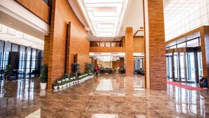 Un amplio vestíbulo con suelo de mármol pulido, detalles de madera y una escalera central.